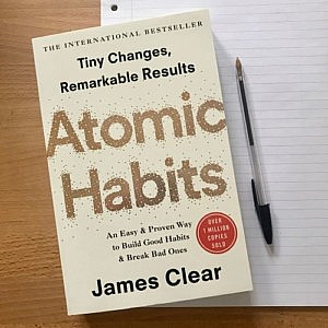 The book &quot;Atomic Habits&quot; and a notebook and pen on a desk