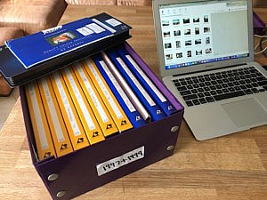 a box of organised photos and laptop on a desk