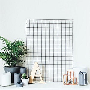 An organised white desk with a plant, vases and gold A ornament against a wire grid noticeboard and white wall