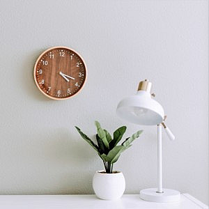 Clock on a white wall above a white desk plant and lamp